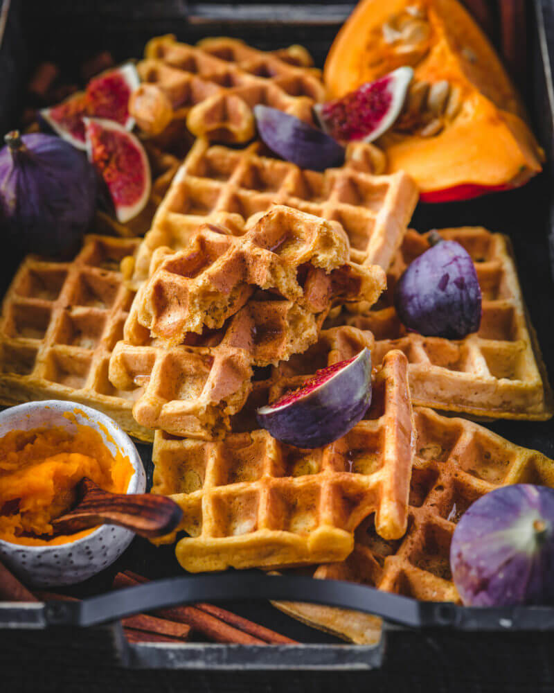 Vegane Kürbis-Waffeln auf dunklem Hintergrund, dekoriert mit Feigen und Kürbisstückchen