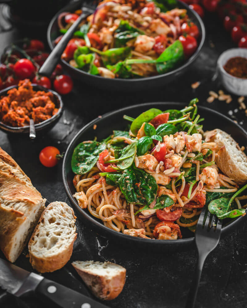 Selbstgemachter Spaghettisalat mit Pesto, Spinat und Mozzarella angerichtet in einem tiefen Teller auf dunklem Hintergrund