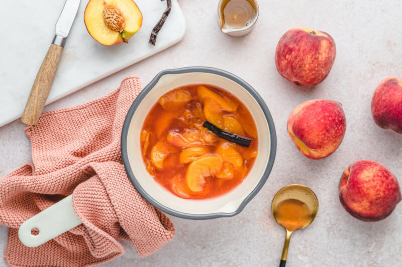 Ein Topf gefüllt mit Zucker, Pfirsichen und einer Vanilleschote - alles wird zu einem süß-fruchtigen Sirup eingekocht